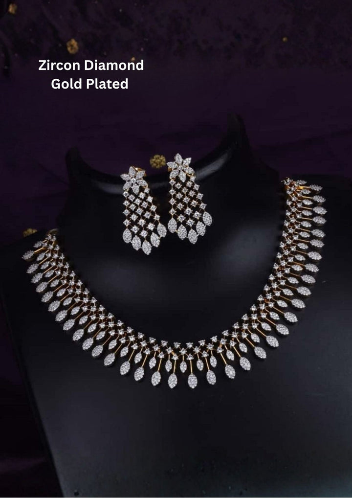 Elegant zircon diamond gold plated necklace set featuring a graceful collar-style necklace adorned with sparkling white zircon stones and cascading leaf-shaped dangling motifs. The matching statement earrings showcase a floral-inspired top with intricate stone-studded lattice detailing and shimmering leaf drops, creating a luxurious and sophisticated look suitable for weddings, receptions, parties and festive occasions.