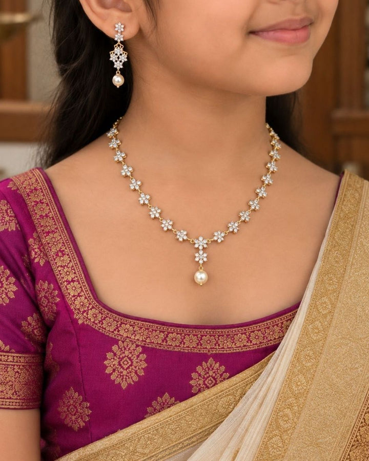Gold plated diamond replica necklace set featuring delicate floral motifs, sparkling stones, and matching drop earrings with pearl accents, displayed on a maroon jewellery bust.