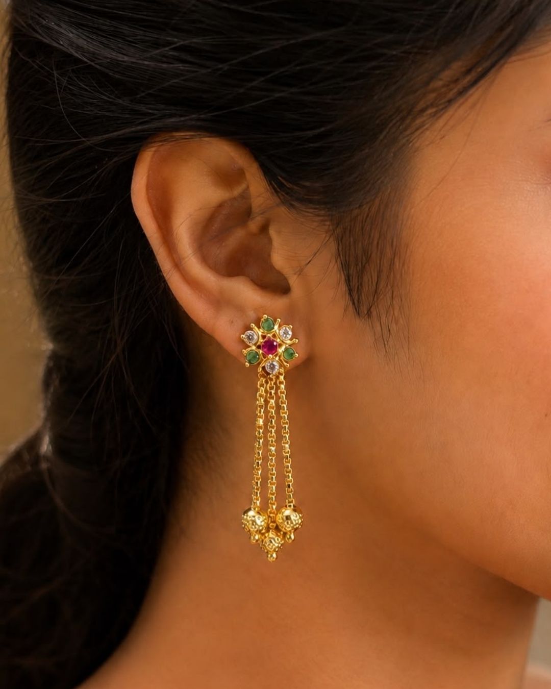 Stylish gold plated long drop earrings featuring vibrant ruby and green stones, sparkling white accents, intricate gold detailing, multiple hanging chains, and decorative gold ball drops. Perfect for festive occasions, traditional outfits, weddings, parties, and special events.