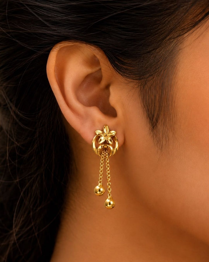 Stylish gold plated floral drop earrings featuring a detailed flower motif, elegant circular design, delicate hanging chains, and polished gold ball drops. Perfect for everyday wear, festive occasions, traditional outfits, parties, and special events.