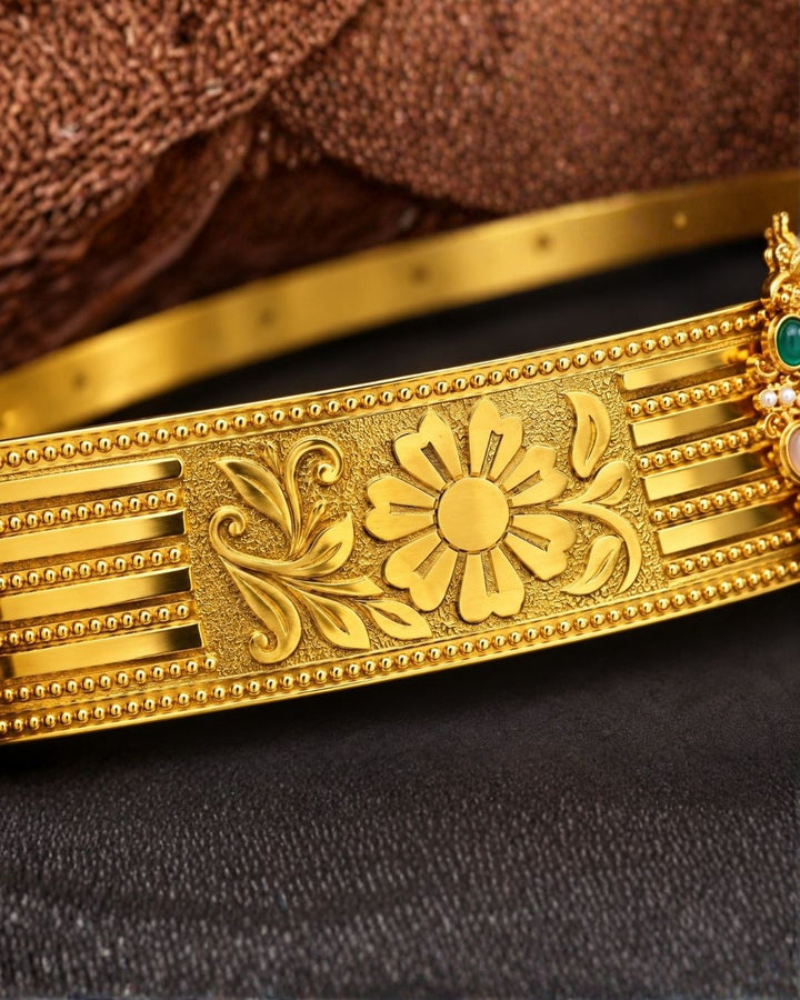 Beautiful gold plated kids hip belt featuring an intricately engraved wide band with floral designs and a central Ganesha motif surrounded by colorful green, red, blue, and white stones. Perfect for girls&