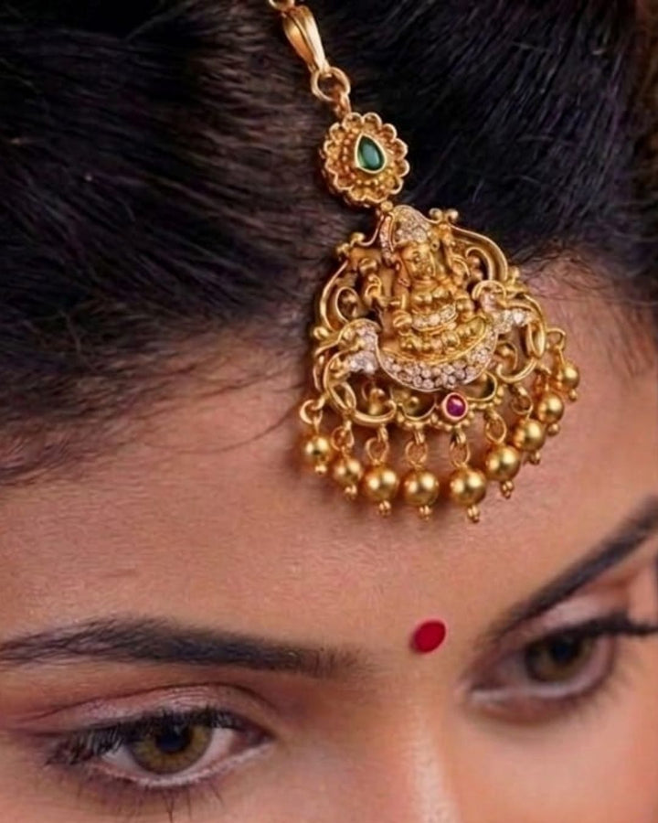 Beautiful traditional gold plated temple pendant featuring an intricate divine motif, ornate filigree detailing, sparkling white stone accents, a green stone accent at the top, and multiple dangling gold bead drops. Perfect for festive occasions, temple visits, traditional outfits, weddings, and spiritual gifting.