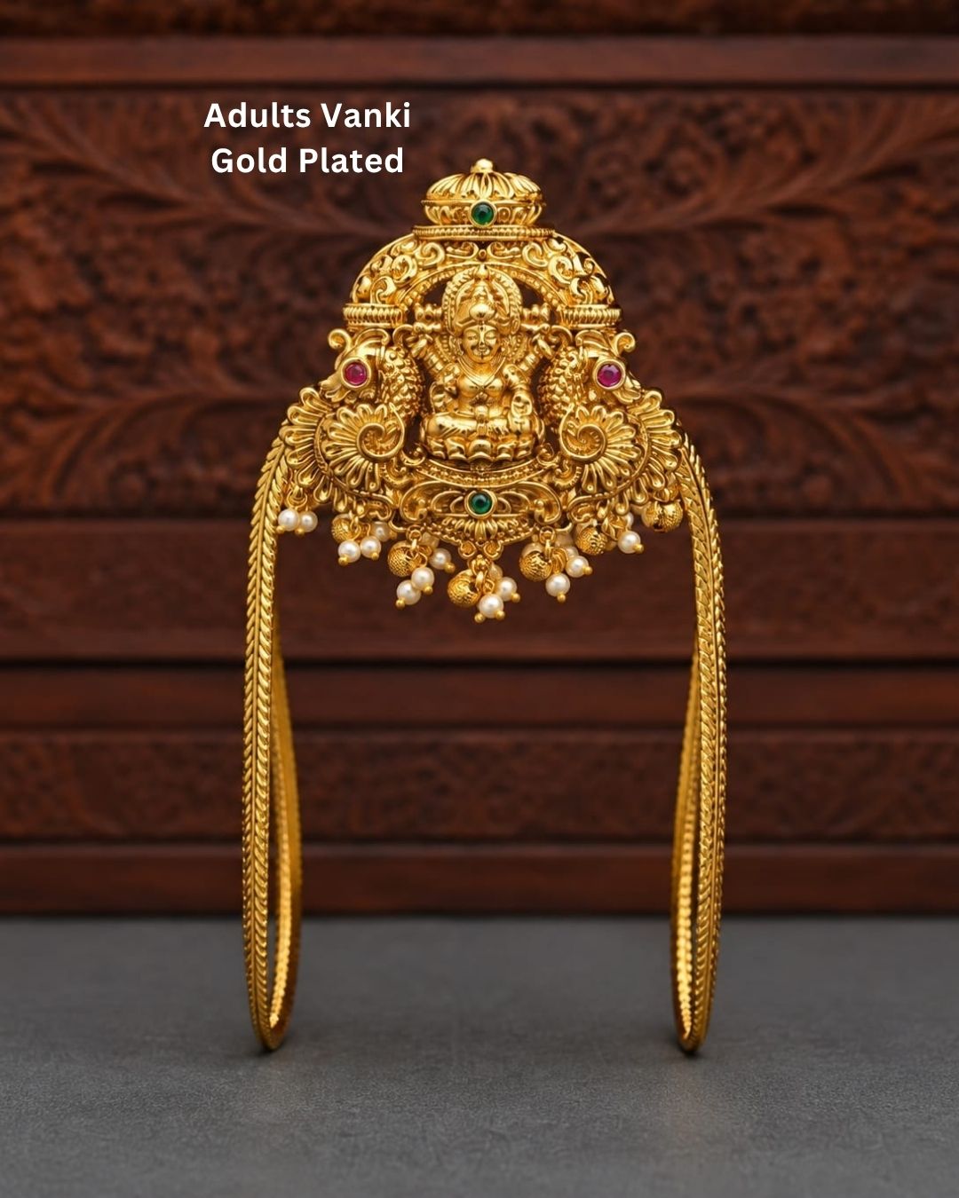 Traditional gold plated Vanki armlet featuring an ornate Goddess Lakshmi design, intricate floral detailing, green and red stone accents, and delicate pearl and gold bead hangings.