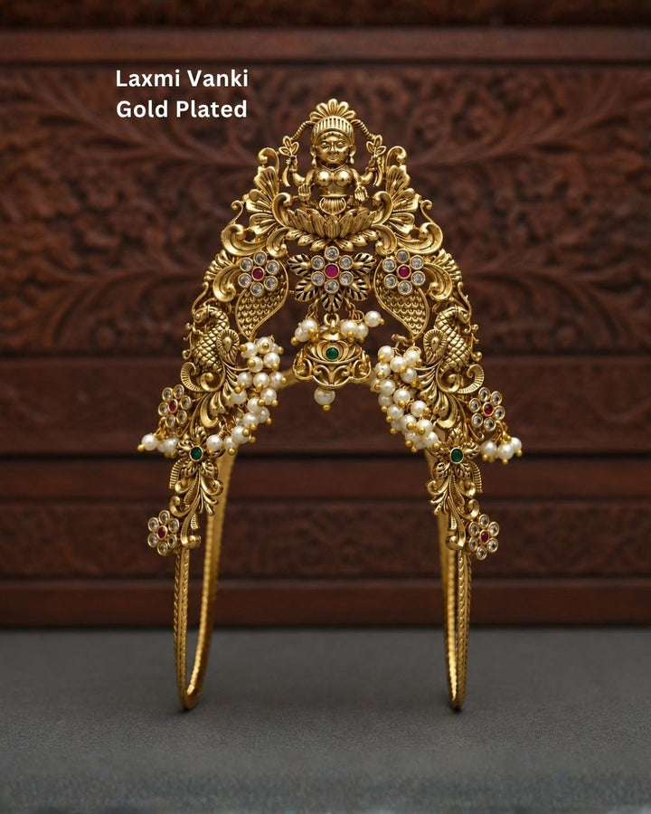 Beautiful Lakshmi Vanki gold plated armlet featuring an ornate Goddess Lakshmi design, peacock-inspired motifs, green and ruby-colored stones, and pearl detailing. Perfect for traditional outfits, festive occasions, temple events, weddings, and gifting.