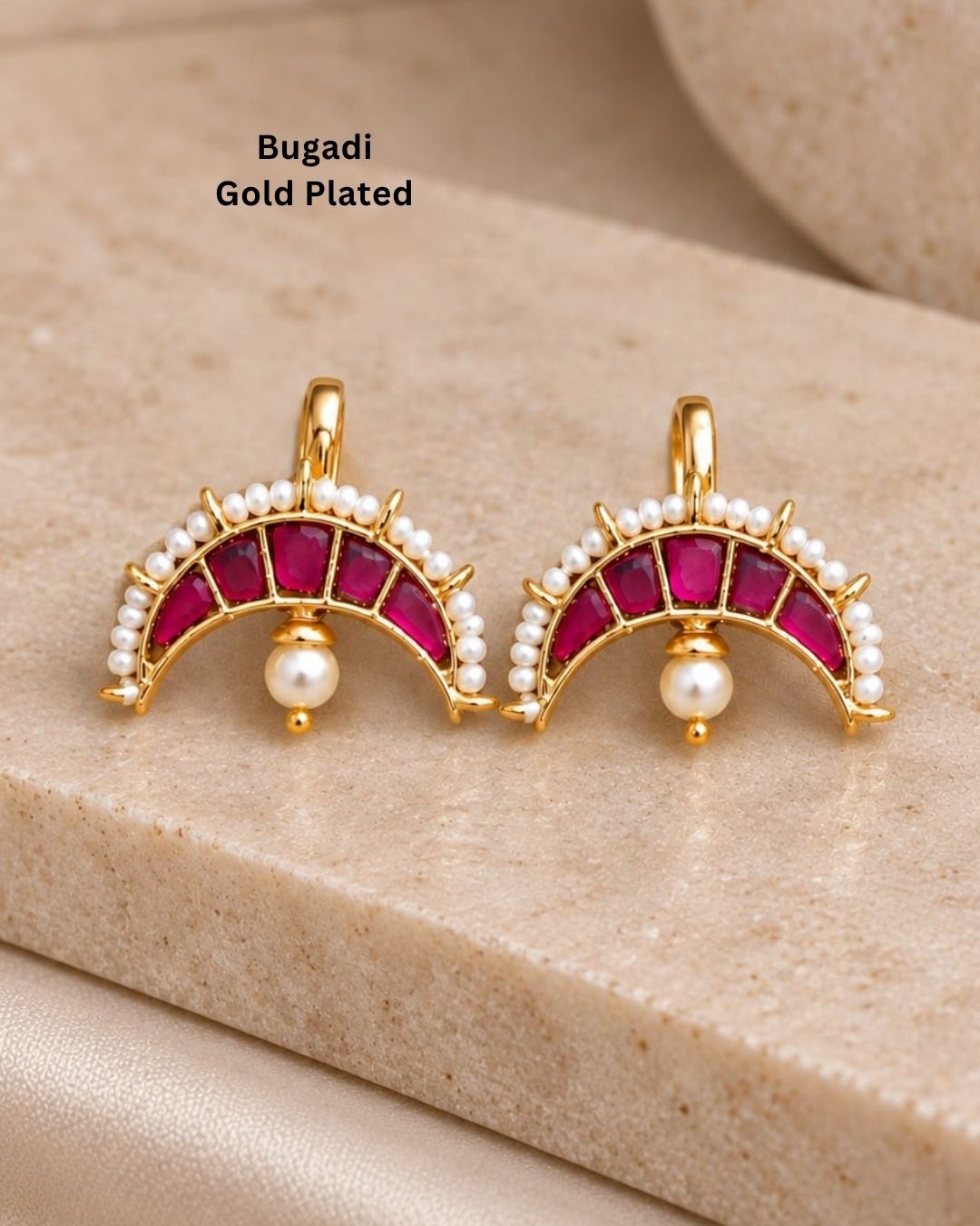 Premium gold plated bugadi earrings featuring an elegant half-moon design embellished with ruby-colored stones, a pearl border, and delicate hanging pearl drops. Perfect for weddings, festive occasions, traditional wear, parties, and gifting.