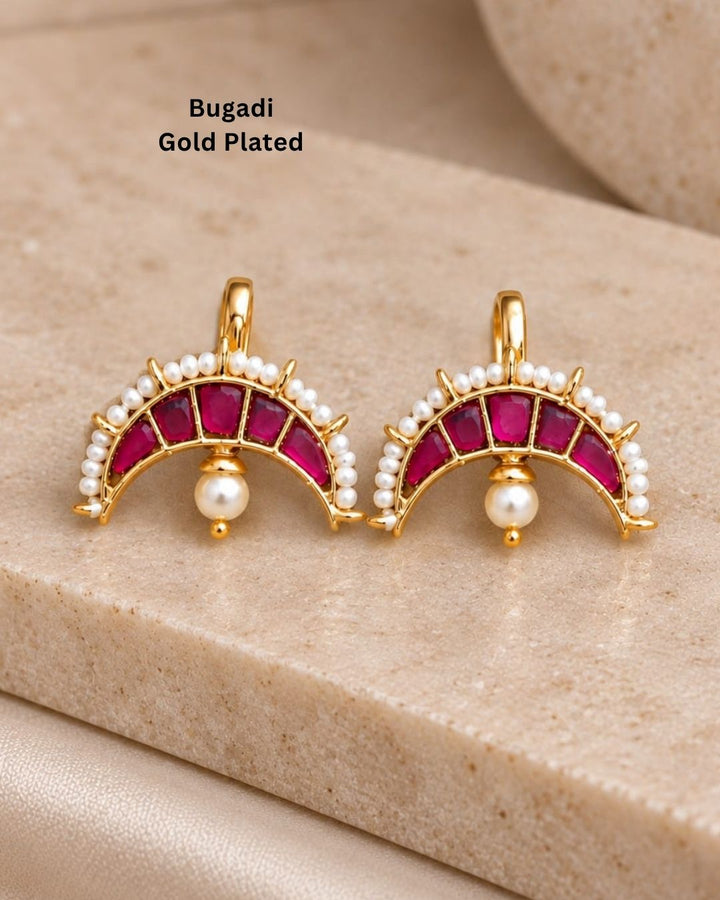 Premium gold plated bugadi earrings featuring an elegant half-moon design embellished with ruby-colored stones, a pearl border, and delicate hanging pearl drops. Perfect for weddings, festive occasions, traditional wear, parties, and gifting.
