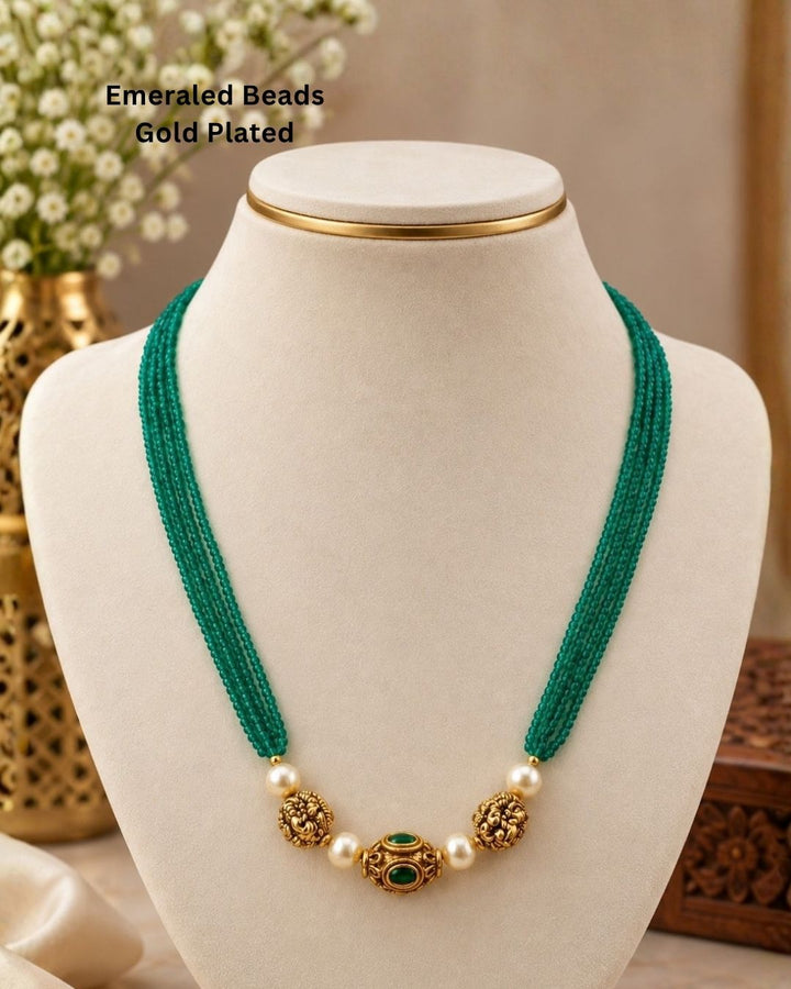 Traditional gold plated emerald beads necklace featuring multiple green bead strands, pearl accents, detailed gold motifs, and an elegant center pendant, perfect for festive and traditional wear.