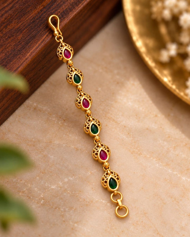Gold plated traditional ear chains featuring alternating red and green teardrop stones with intricate antique gold detailing.