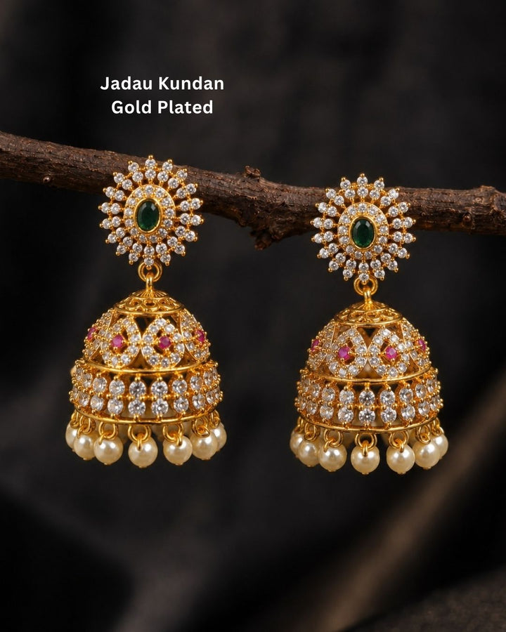 Beautiful gold plated designer jhumka earrings featuring intricate floral detailing, green stones, pink and white stone accents, and a row of elegant pearl drops. Perfect for festive occasions, traditional wear, weddings, and gifting.