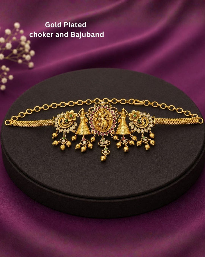Beautiful gold plated 2-in-1 choker and bajuband set featuring Goddess Lakshmi, peacock and floral motifs embellished with green and pink stones and delicate hanging gold beads. Perfect for weddings, festive occasions, traditional wear, Bharatanatyam styling, parties and gifting.