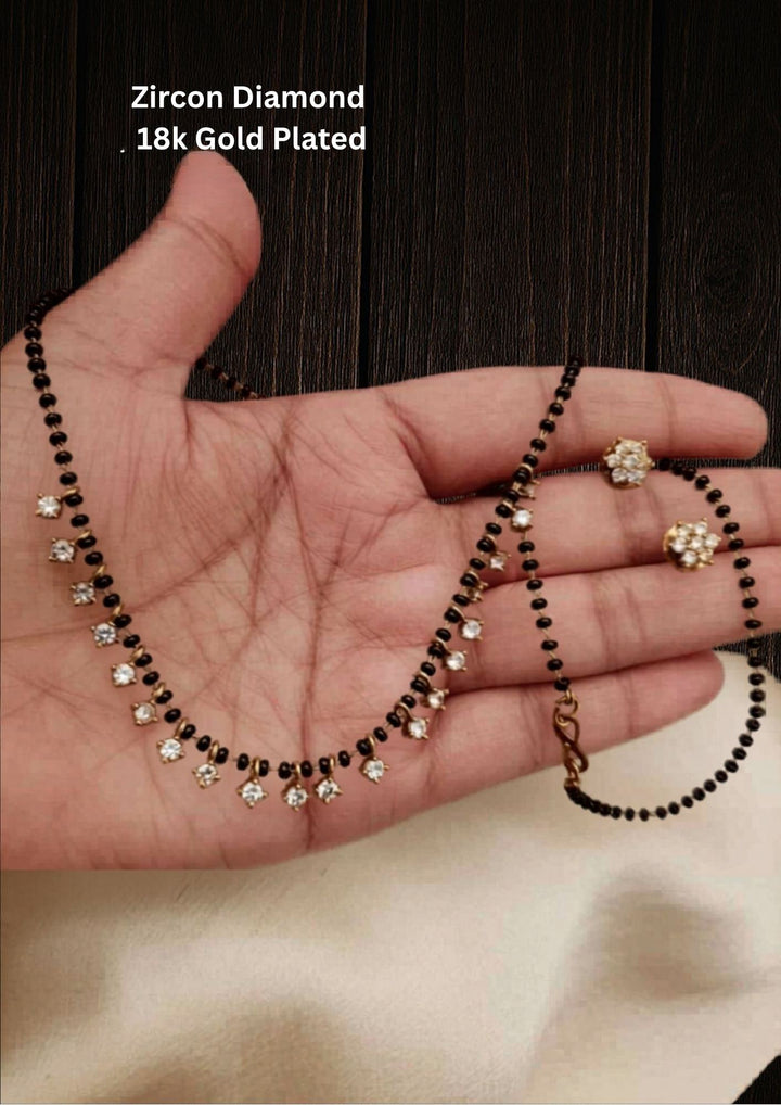 This is a simple and delicate Zircon Diamond Mangalsutra Set with matching earrings. It features a modern, lightweight look designed for everyday wear. The style blends the traditional protective black beads with trendy hanging charms.