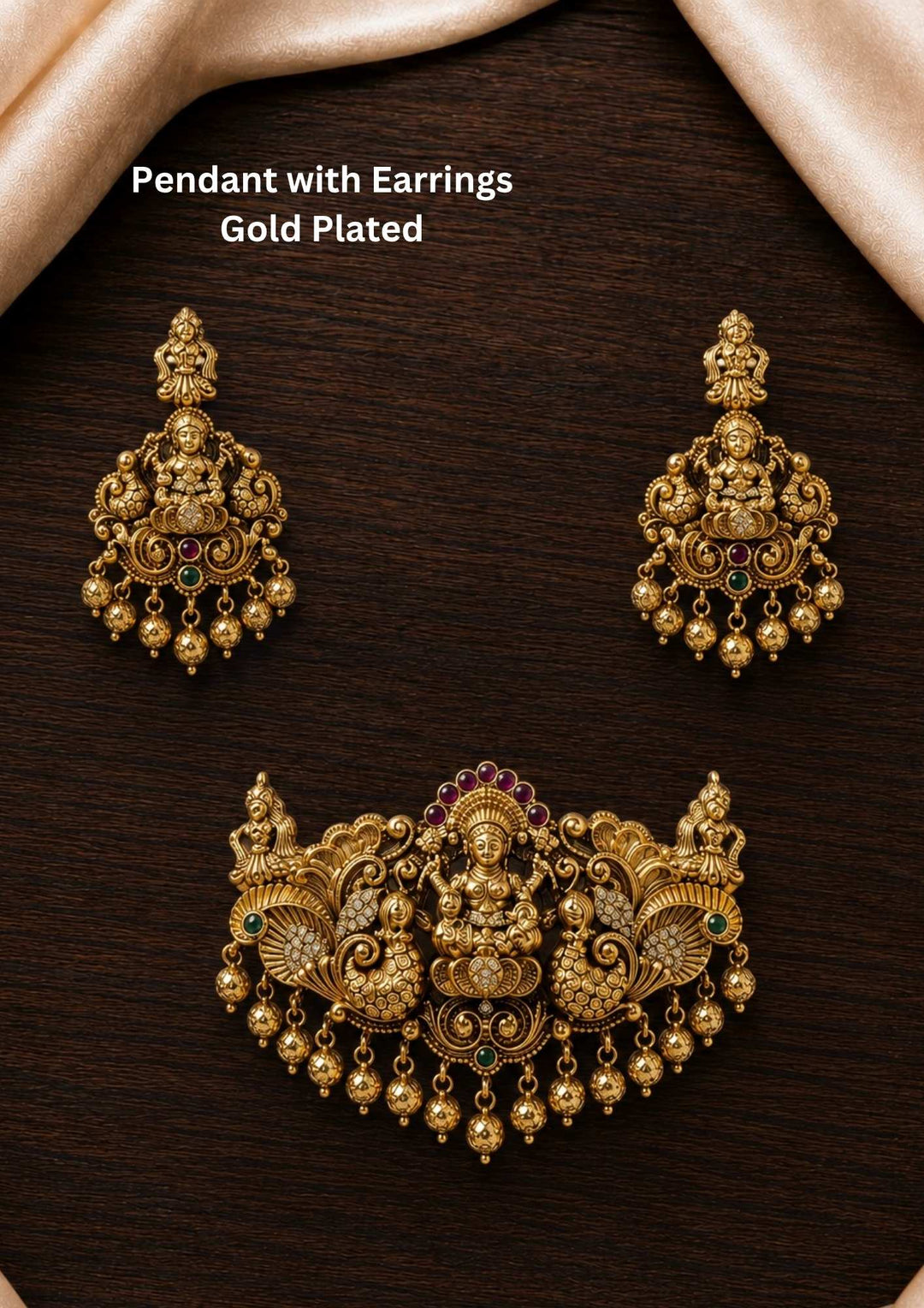 A traditional gold plated temple jewelry set in image_d00629.png featuring a grand, broad detachable pendant and matching hanging earrings. The antique-finished pieces are intricately embossed with a seated Goddess Lakshmi motif flanked by detailed peacocks, accented with ruby-pink stone crowns and dangling gold bead drops perfect for weddings, functions, poojas