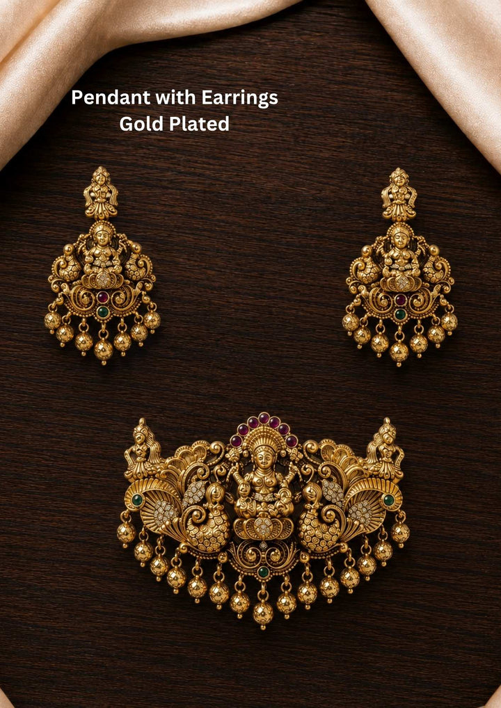 A traditional gold plated temple jewelry set featuring a grand, broad detachable pendant and matching hanging earrings. The antique-finished pieces are intricately embossed with a seated Goddess Lakshmi motif flanked by detailed peacocks, accented with ruby-pink stone crowns and dangling gold bead drops perfect for weddings, functions, poojas