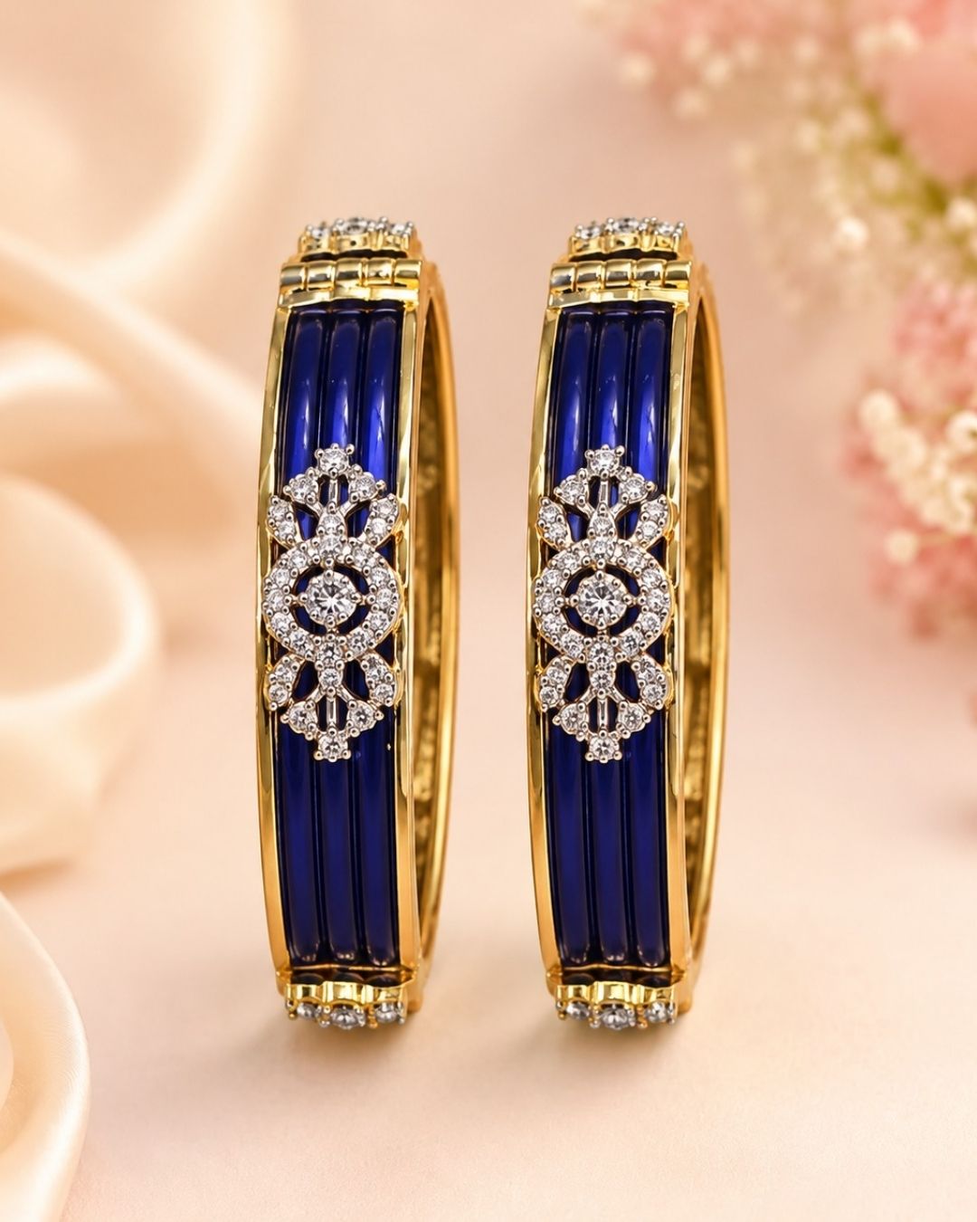Designer gold plated bangles featuring deep blue detailing, sparkling white stone floral motifs, and polished gold borders, perfect for festive, wedding, traditional, and special occasions.