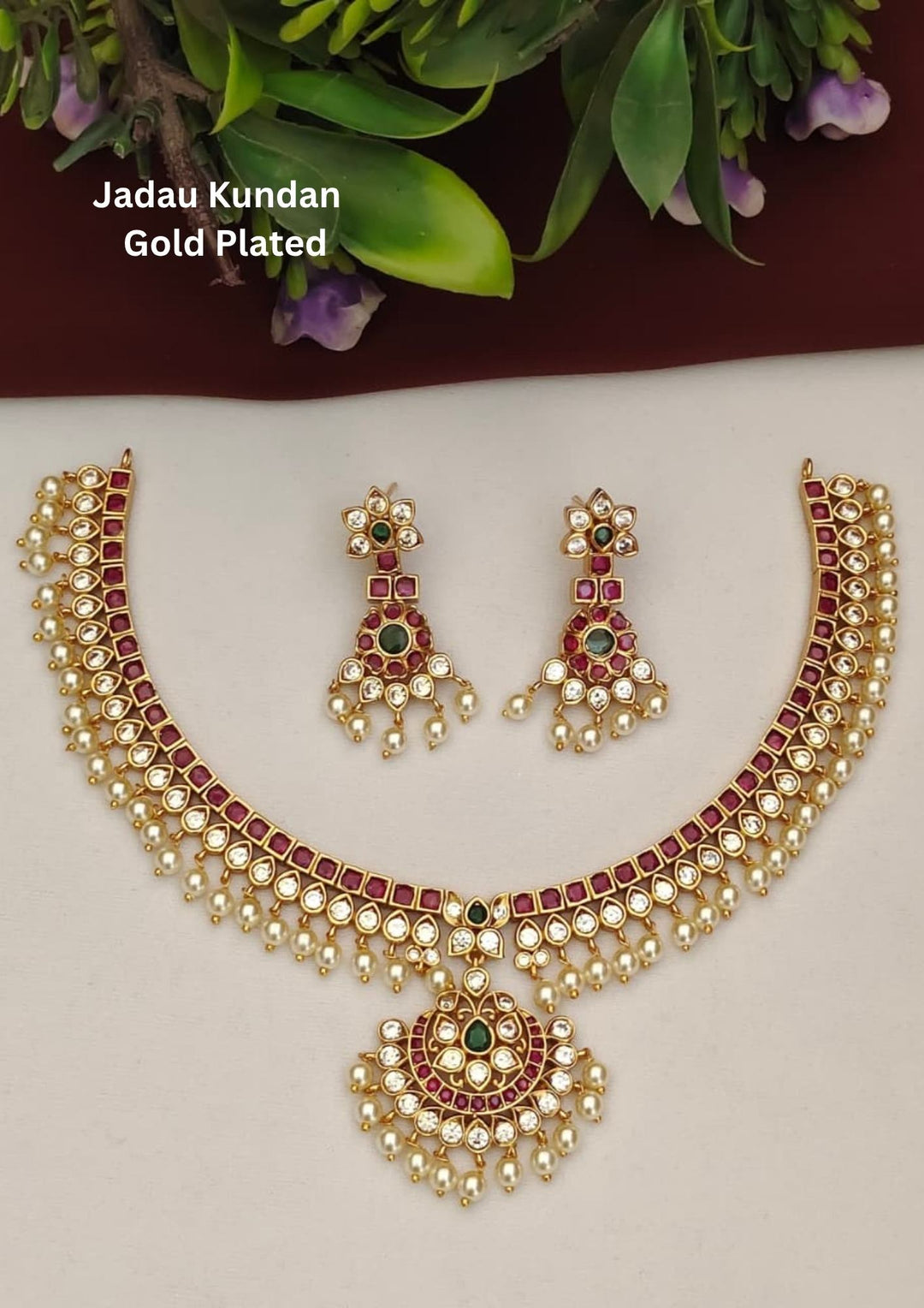Jadau Kundan gold plated necklace set with matching earrings featuring traditional ruby pink square stones, white kundan stones, pearl drop hanging design, floral patterns, antique temple style finish and green stone highlights. This elegant choker necklace is perfect for weddings, bridal wear, poojas, festivals, sarees, lehengas, Bharatanatyam performances and traditional South Indian ethnic outfits with lightweight comfortable fitting, skin friendly quality and Cash on Delivery available.