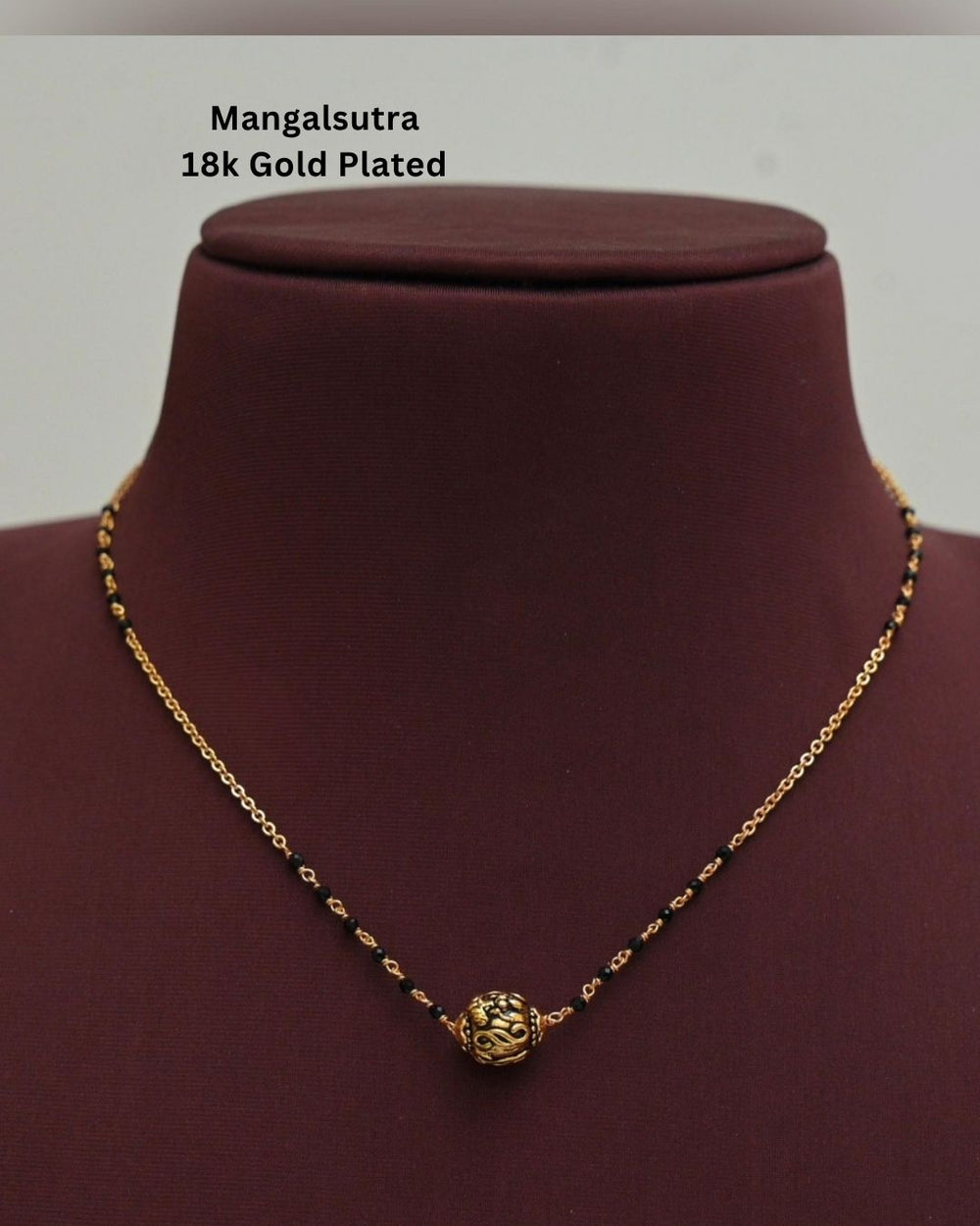 Gold replica black beads necklace featuring a delicate gold-toned chain, black beads, and a round textured gold pendant at the center, displayed on a maroon jewellery bust.