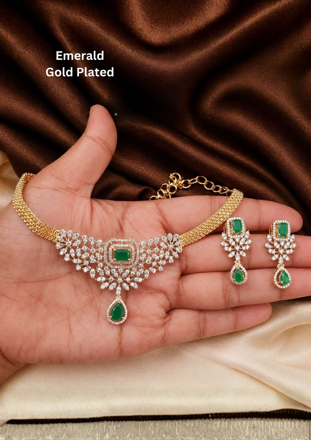 It centers an intricate, V-shaped floral bib pattern encrusted with glittering white American Diamonds (CZ stones), a prominent square emerald-green center stone, and a dangling teardrop emerald charm at the base. Includes a matching pair of elegant hanging earrings featuring a floral design with square and teardrop green stone accents. Perfect for parties and festive occasions with skin-friendly premium quality, comfortable fit,