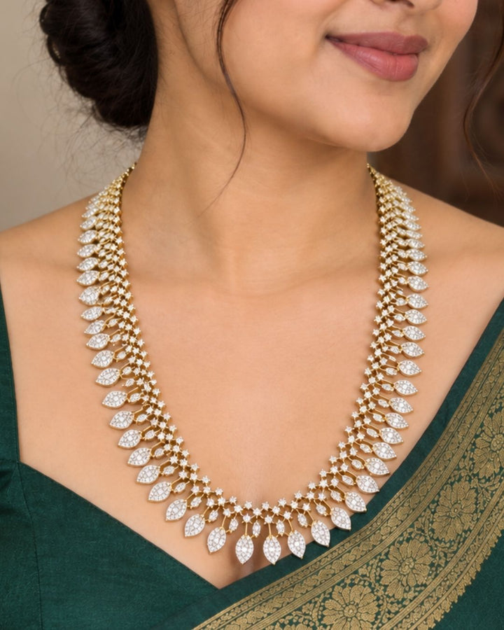 Designer gold plated long necklace and matching earrings featuring intricate leaf motifs embellished with sparkling white stones, perfect for festive, wedding, and traditional occasions.