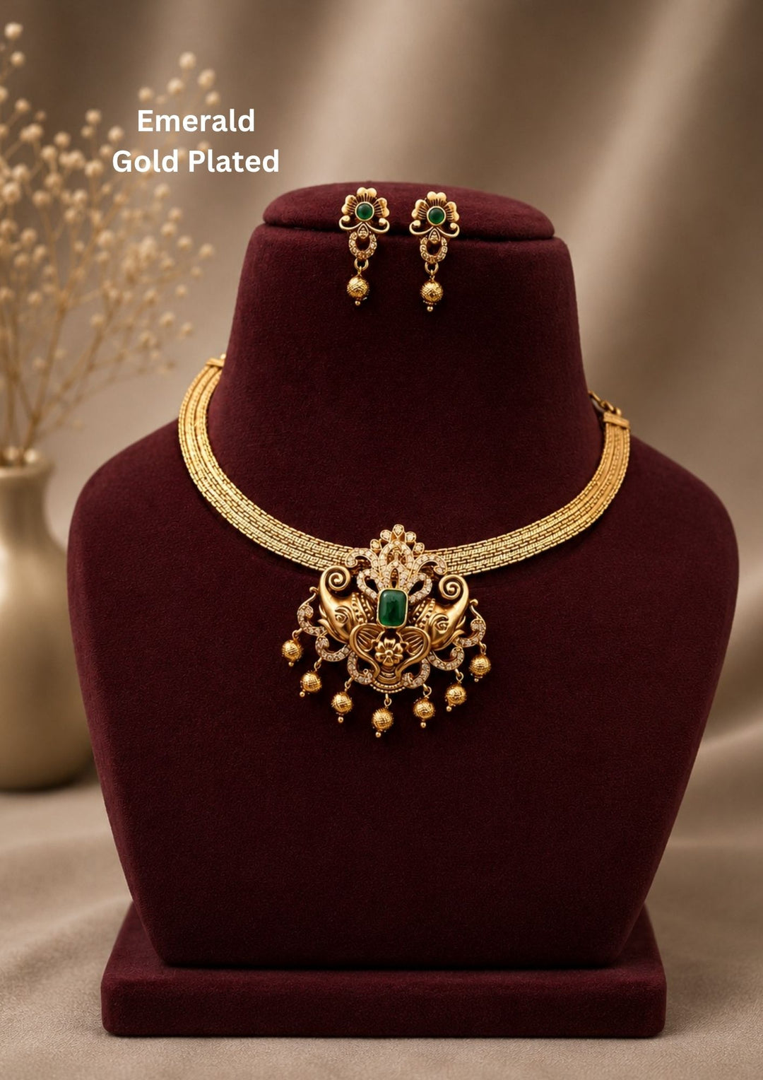 Designed with a flexible gold-mesh choker chain paired with an intricate, detachable pendant. The antique-finished pendant showcases a center emerald-green stone flanked by two detailed elephant motifs, highlighted with sparkling white stones and a fringe of dangling gold beads. Includes a matching pair of floral-top hanging earrings with green accents and gold drops. Perfect for festive events, featuring premium quality and Cash on Delivery available.