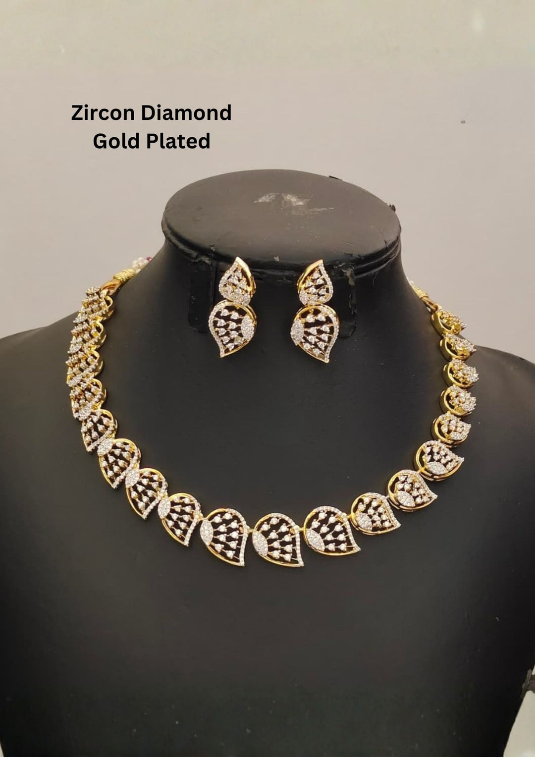 Gold plated jewelry set  featuring a delicate choker necklace made of repeating, stylized leaf or paisley-shaped links. Each openwork link is encrusted with brilliant, clear white Zirconian diamonds (American Diamonds) that catch the light beautifully. Includes a matching pair of elegant hanging earrings mimicking the exact leaf pattern. Crafted for festive occasions and parties with premium quality and Cash on Delivery available.