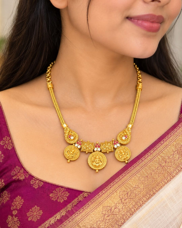 Traditional gold plated designer necklace and earrings set featuring multiple Goddess Lakshmi coin motifs, intricate temple-inspired detailing, ruby-colored stone accents, and matching decorative earrings, perfect for festive, wedding, and traditional occasions.
