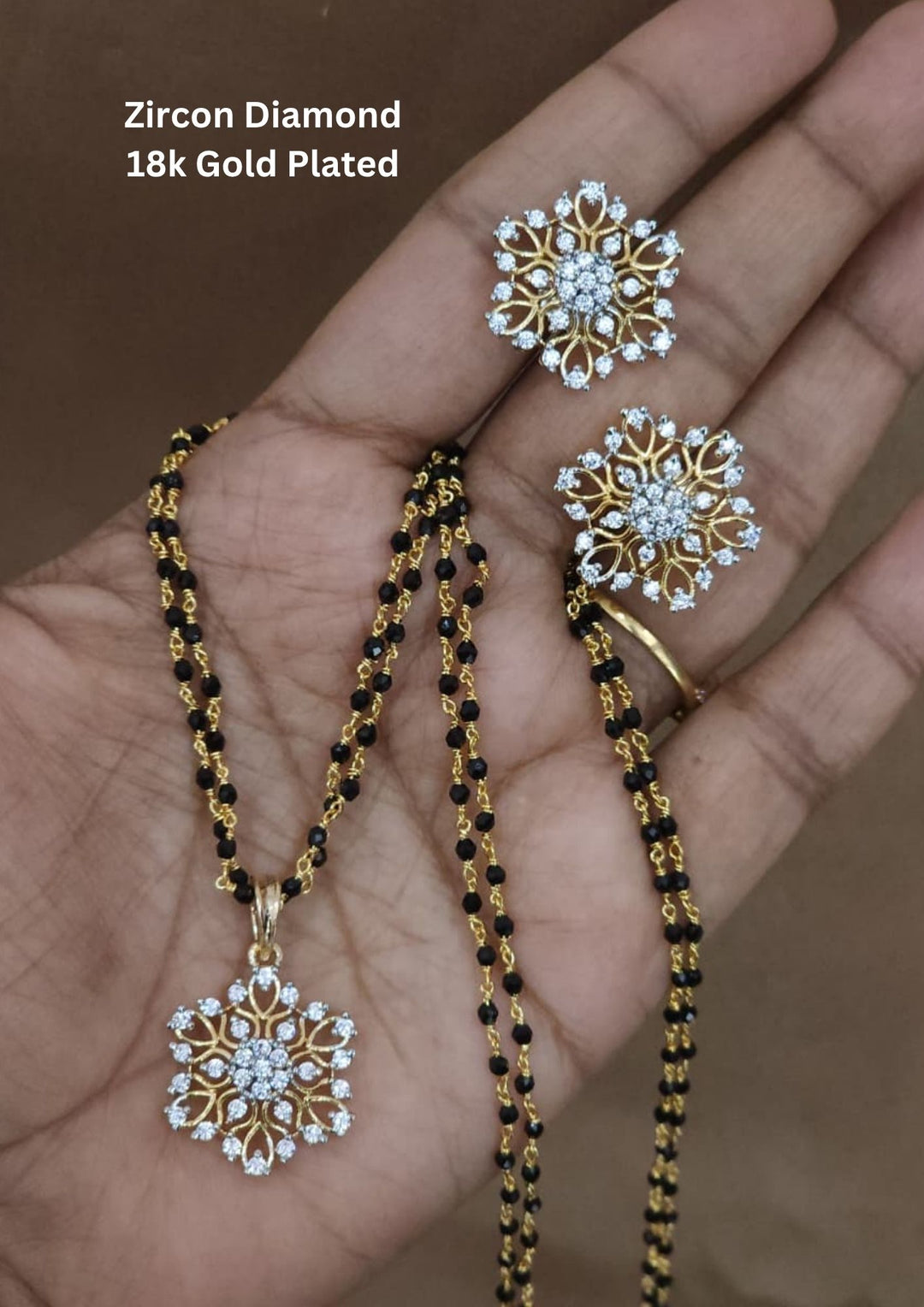 Elegant gold plated mangalsutra set featuring a floral zircon pendant with matching stud earrings. Crafted with a traditional black beaded chain and sparkling crystal stones for everyday elegance and festive wear. Perfect for daily wear, festive occasions and office wear.