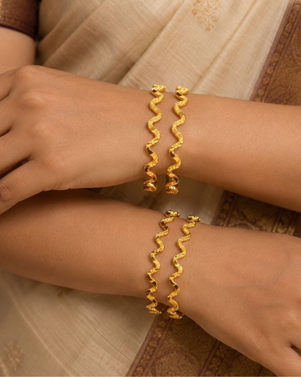 A gold-plated Jadau Kundan maang tikka with intricate floral and paisley motifs, embellished with white faux pearls, pink gemstones, and green stones, displayed on a beige surface with a dark red fabric accent.