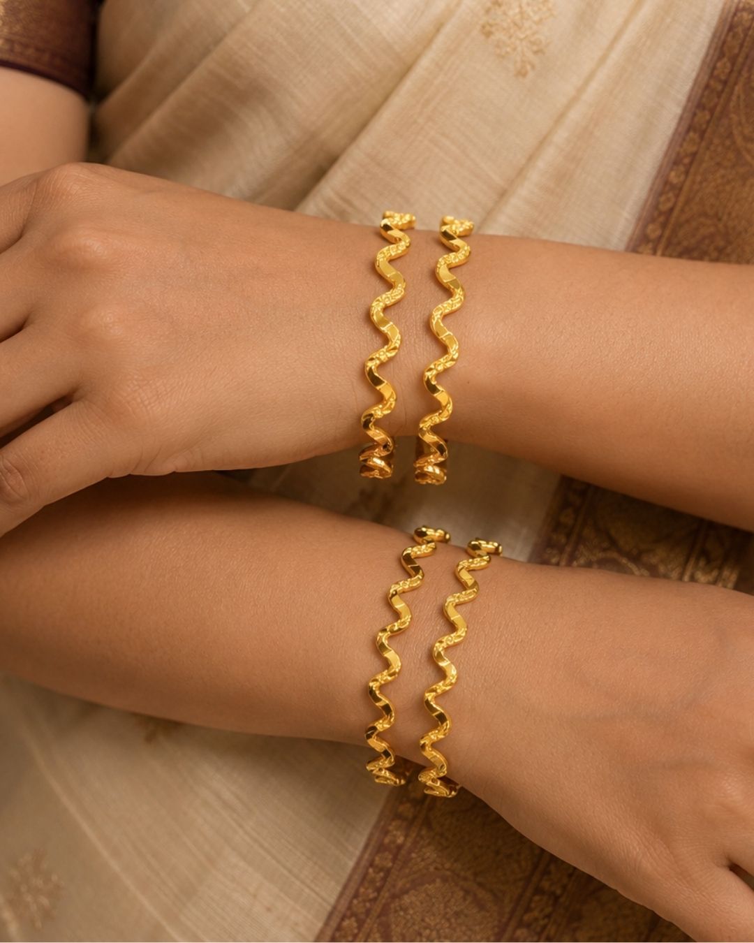 A gold-plated Jadau Kundan maang tikka with intricate floral and paisley motifs, embellished with white faux pearls, pink gemstones, and green stones, displayed on a beige surface with a dark red fabric accent.