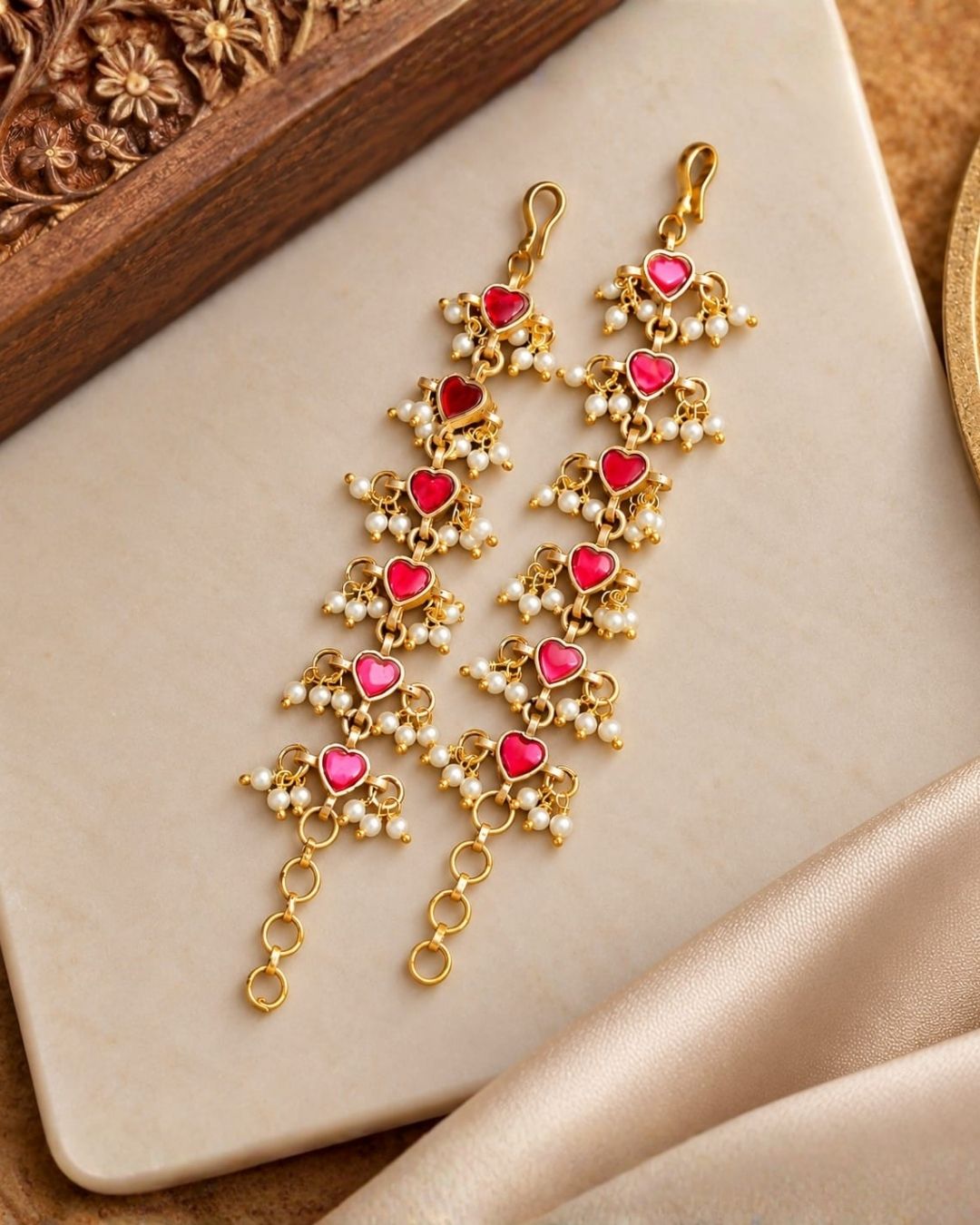 Pair of gold plated designer ear chains with repeating pink heart motifs, white pearl embellishments, and circular adjustment links.