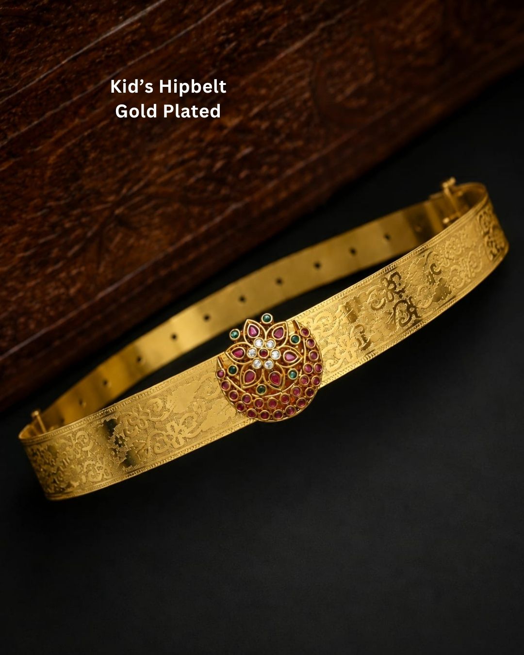 Beautiful gold plated hip belt featuring an intricately engraved wide band with a floral gemstone centerpiece accented with ruby, green, and white stones. Perfect for traditional wear, weddings, festive occasions, bridal styling, parties, and gifting.