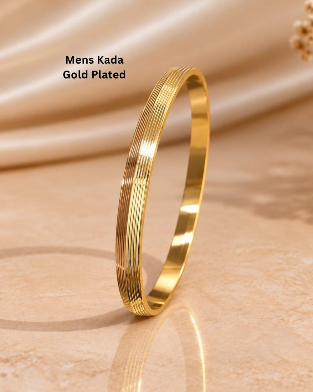Stylish men’s gold plated kada displayed upright on a warm beige surface with a premium minimal background.