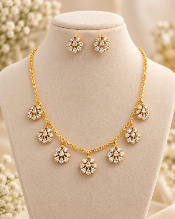 Elegant gold plated necklace with sparkling white zircon stones and floral dangling motifs displayed on a navy blue jewellery bust.