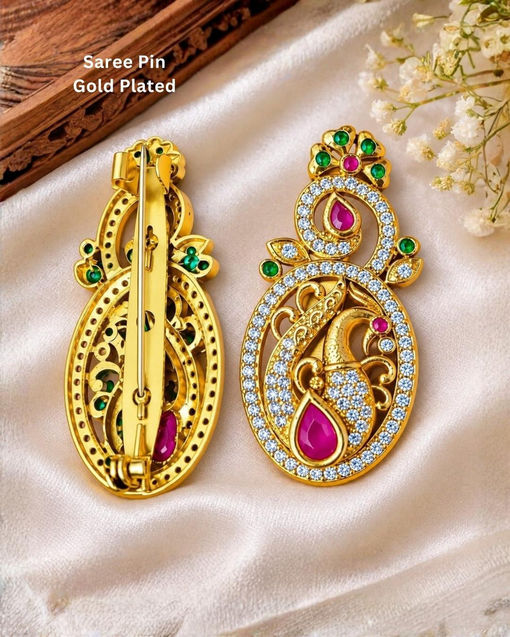 Pair of gold plated peacock design saree pins displayed on a light wooden surface, showing decorative front designs and secure pin-back fastenings.