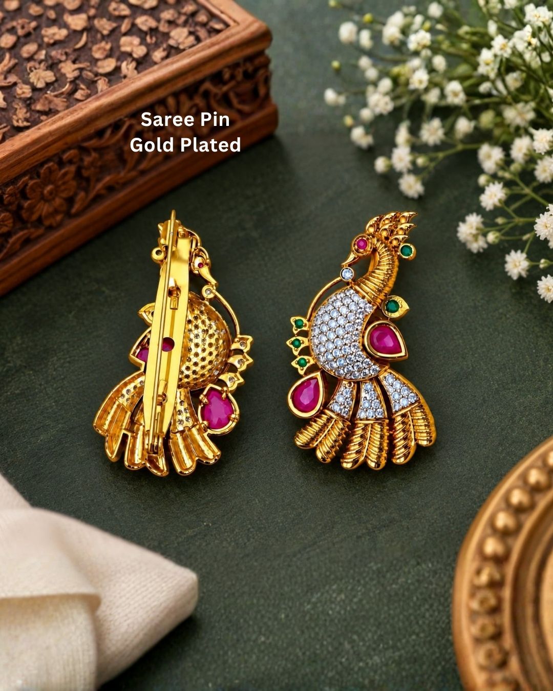 Pair of gold plated peacock saree pins displayed on a light wooden surface, showcasing detailed craftsmanship and decorative stone embellishments.