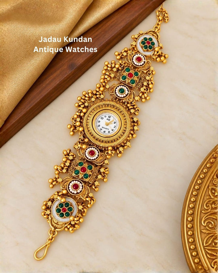Traditional gold plated jewellery watch displayed diagonally on a cream surface with a wooden accent and gold decorative details.