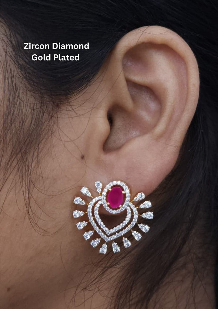 Close-up of an ear wearing a zircon diamond gold-plated earring with a red gemstone.