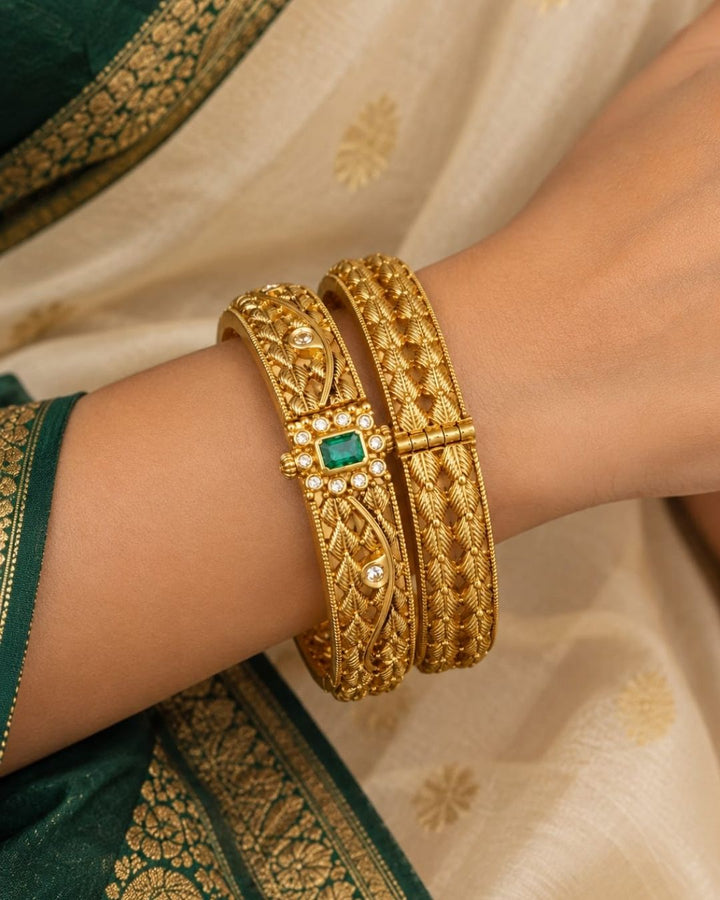 Traditional gold plated designer bangles featuring intricate layered leaf motifs, sparkling white stone embellishments, and a vibrant green center stone, perfect for festive, wedding, and traditional occasions.