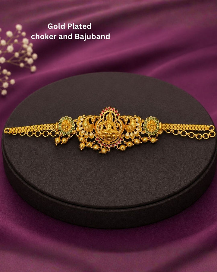 Beautiful traditional 2 in 1 gold plated choker and bajuband set featuring a detailed Goddess Lakshmi centerpiece, ornate peacock motifs, sparkling white stones, red and green accents and elegant gold bead drops.