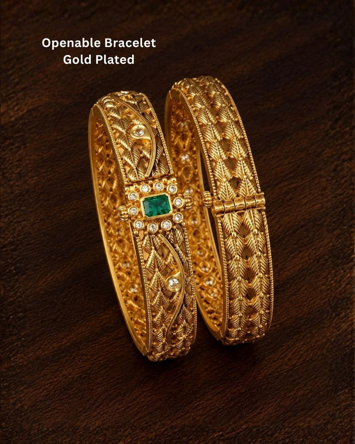 Traditional gold plated designer bangles featuring intricate layered leaf motifs, sparkling white stone embellishments, and a vibrant green center stone, perfect for festive, wedding, and traditional occasions.