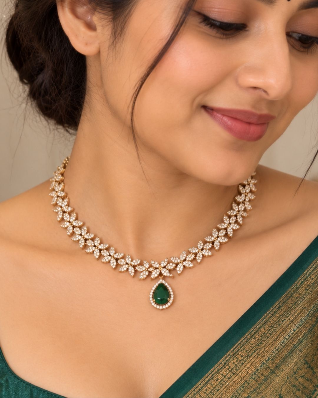 Designer gold plated necklace and earrings set featuring a delicate arrangement of leaf-shaped motifs embellished with sparkling white stones, a prominent green teardrop pendant, and matching green stone drop earrings, perfect for festive, wedding, and elegant occasions.