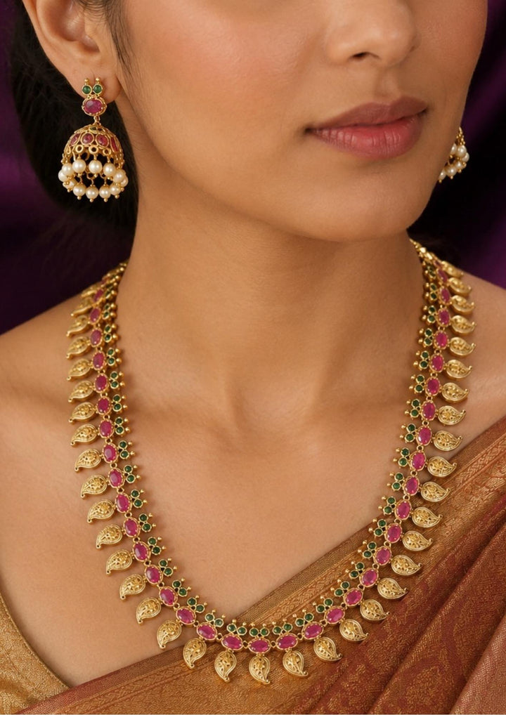 Traditional jadau kundan gold plated necklace set featuring intricate floral motifs adorned with vibrant pink and green stones along with elegant pearl drops. The matching statement earrings enhance the ethnic charm, creating a luxurious and festive jewelry design perfect for weddings and traditional celebrations.