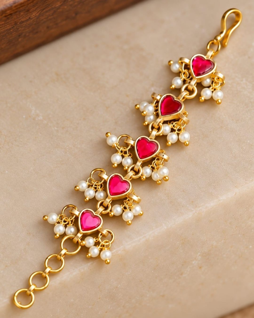 Pair of gold plated designer ear chains with repeating pink heart motifs, white pearl embellishments, and circular adjustment links.