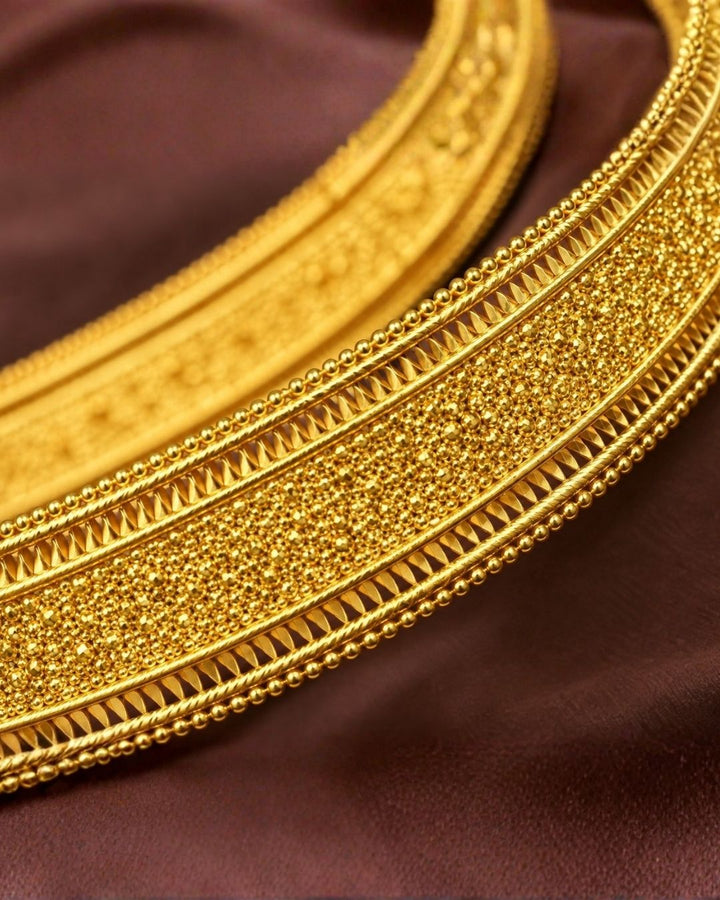 South Indian Women Wearing a gold plated traditional adult hipbelt (vaddanam) featuring a wide, flexible band with a shimmering stardust textured finish. The central statement ornament is a large, ornate filigree frame heavily encrusted with white zircon stones, anchoring a rich rectangular emerald green core gemstone.