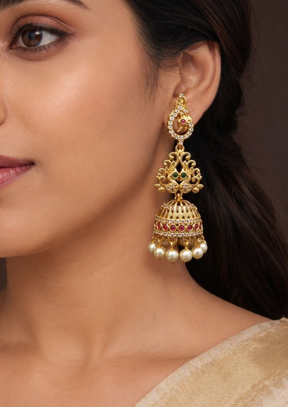south indian women's wear gold-plated Jadau Kundan earrings  a pair of sleek gold  Jhumkas with a peacock modern design. The pattern alternates between Peral drop's Jhumkas shiny gold blocks and blocks filled with sparkling white crystals.