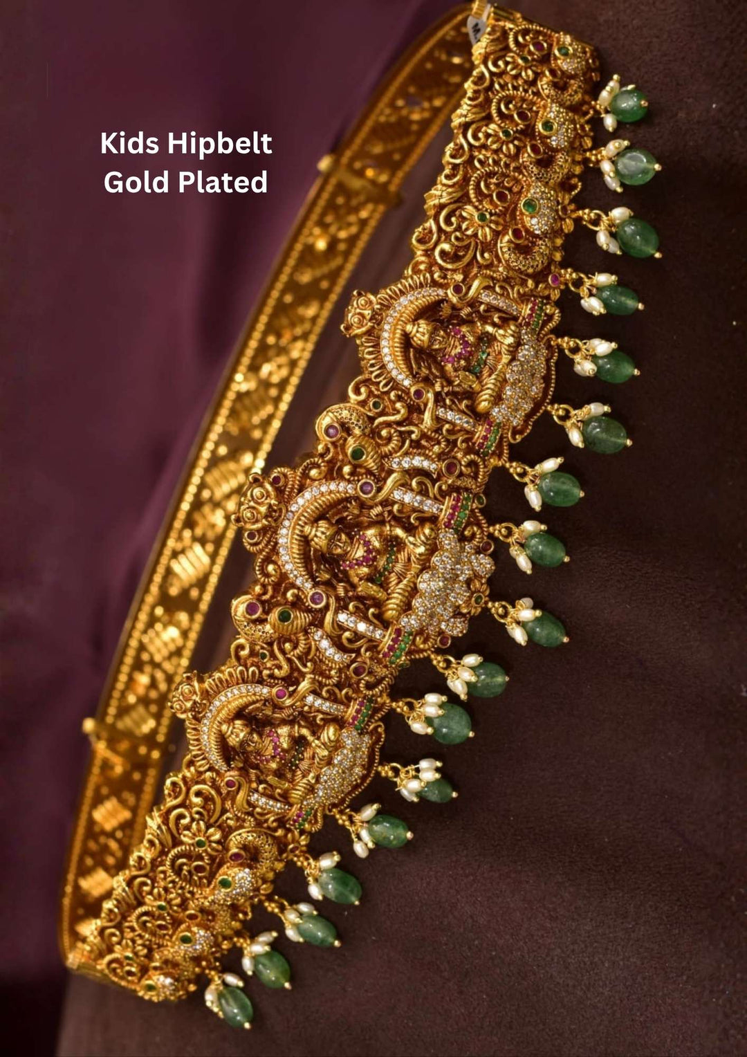 Gold Plated Kundan Beads Laxmi Devi Kids Hipbelt  designed with three laxmi devi motifs and completed with cubic zirconia and the hangings are of kundan beads in green color and it come in anti tarnish color and perfect for weddings, festivals, Bharatnatyam.