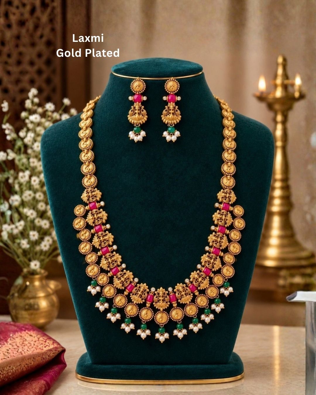 Elegant gold plated Lakshmi coin haram with detailed temple motifs, green beads, pearl drops, and matching Lakshmi earrings displayed on a teal jewellery bust.