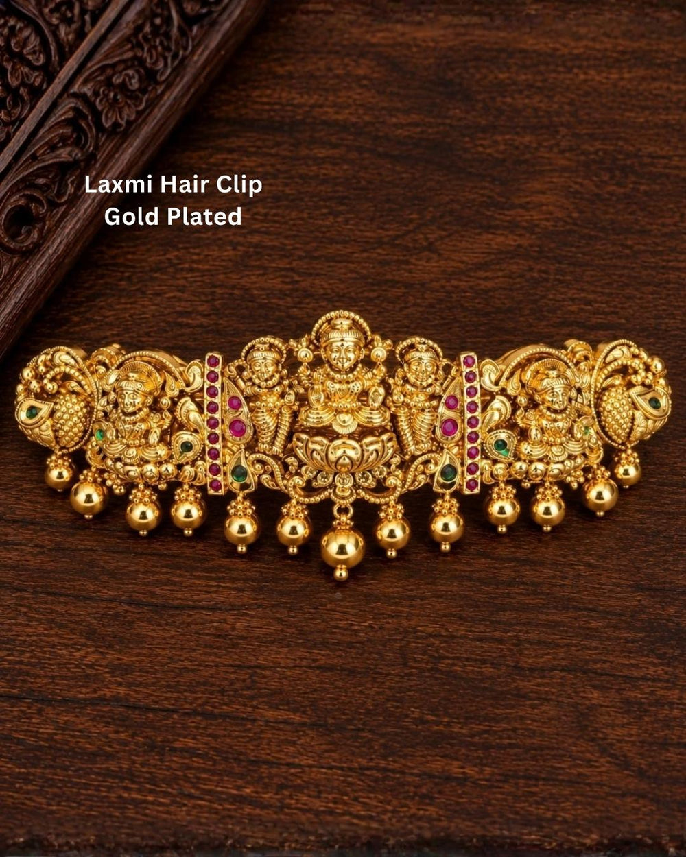 Traditional gold plated designer hair clip featuring multiple Goddess Lakshmi motifs, peacock details, green and ruby-colored stones, intricate floral work, and hanging gold bead embellishments, perfect for festive and traditional hairstyles.