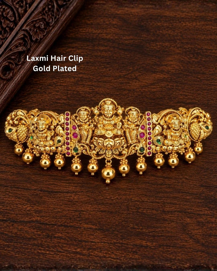 Traditional gold plated designer hair clip featuring multiple Goddess Lakshmi motifs, peacock details, green and ruby-colored stones, intricate floral work, and hanging gold bead embellishments, perfect for festive and traditional hairstyles.