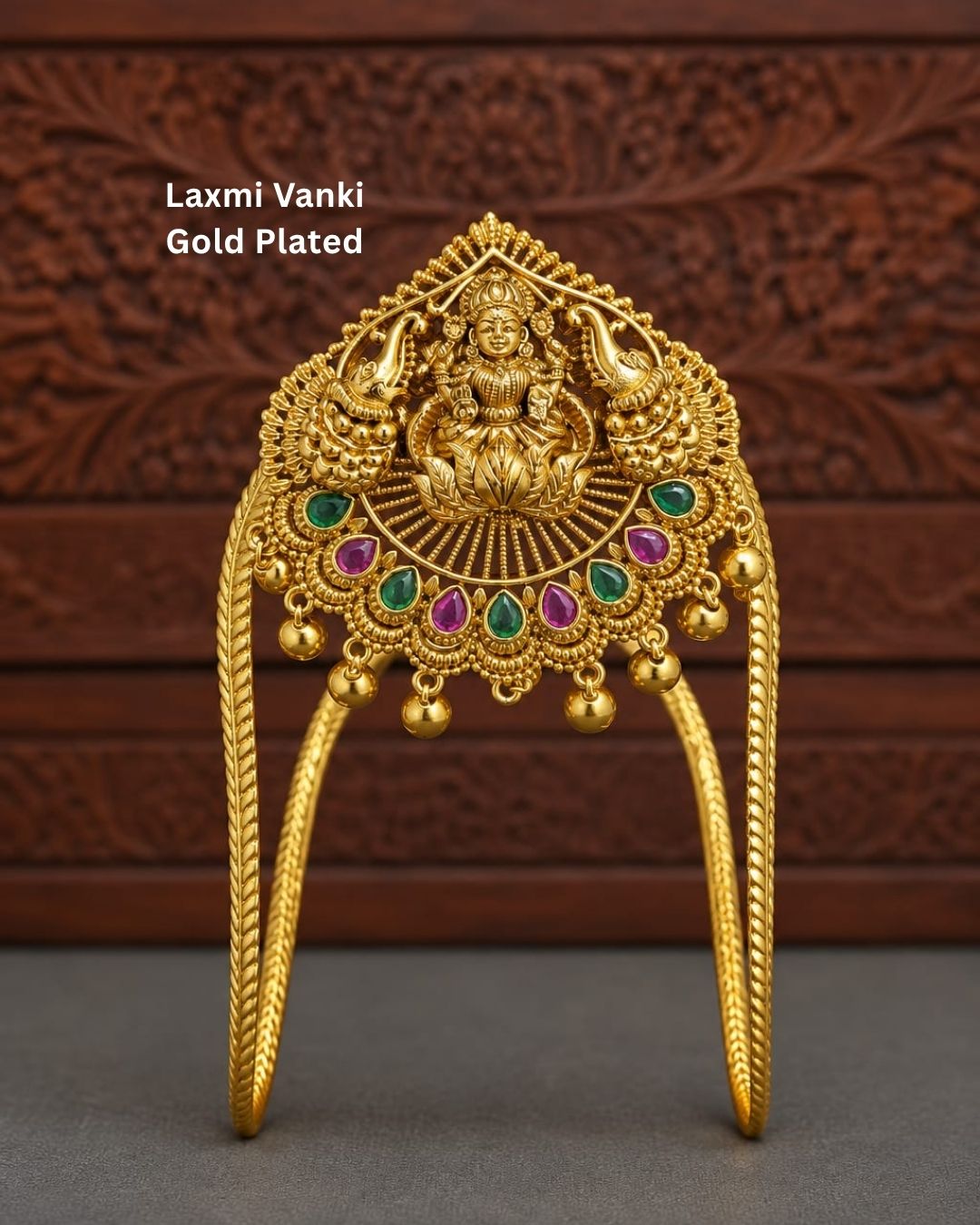 Traditional gold plated designer vanki featuring a detailed Goddess Lakshmi centerpiece, peacock motifs, alternating green and ruby-colored stones, intricate temple-inspired detailing, and hanging gold beads, perfect for festive and wedding occasions.