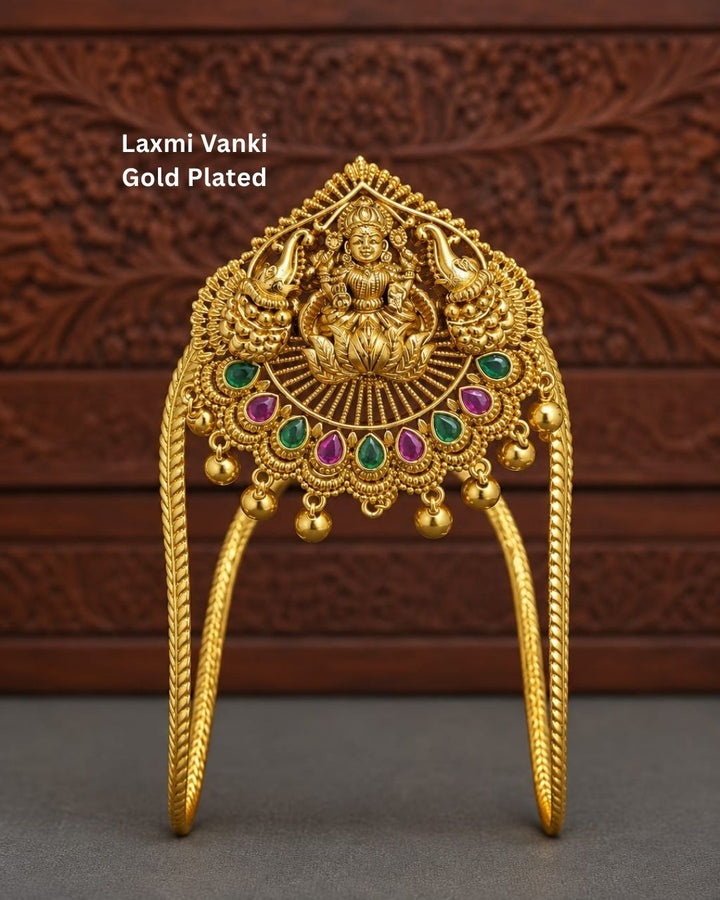 Traditional gold plated designer vanki featuring a detailed Goddess Lakshmi centerpiece, peacock motifs, alternating green and ruby-colored stones, intricate temple-inspired detailing, and hanging gold beads, perfect for festive and wedding occasions.
